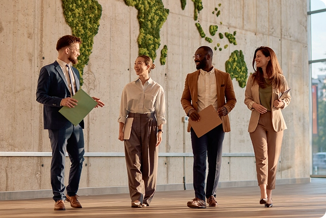 Vier lächelnde Menschen gehen durch eine moderne Büro-Lobby und unterhalten sich in einer professionellen und freundlichen Atmosphäre.