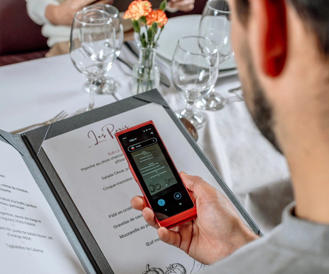Ein Mann in einem eleganten Restaurant, der die Speisekarte mit Hilfe der Foto-Übersetzungsfunktion eines elektronischen Übersetzers liest.