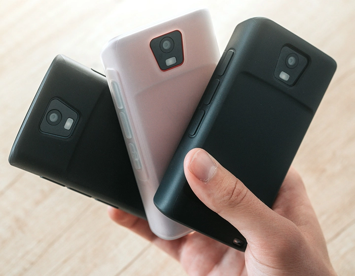 Eine Person hält drei Vasco Translator Q1-Geräte in Schutzhüllen in der Hand, die in drei verschiedenen Farben zu sehen sind: „Solid Black“, „Dark Caramel“ und „Milky White“.